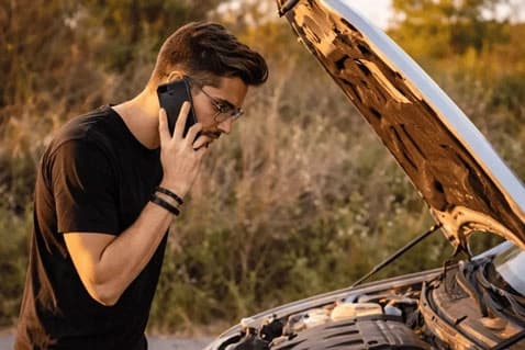 Driver on the phone beside a car with the bonnet open, needing roadside assistance